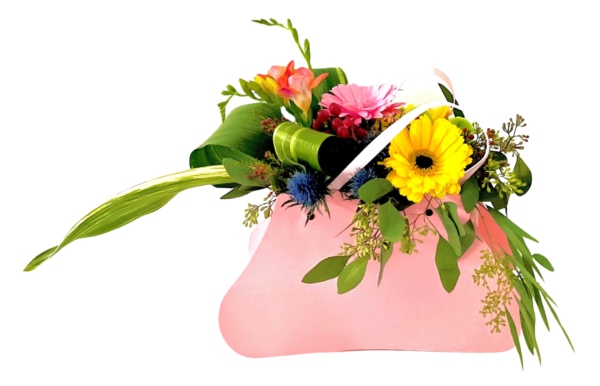 A pink, purse-shaped container holds a vibrant mixed bouquet. A bright yellow gerbera daisy and a soft pink gerbera daisy peek out at center, accompanied by peach freesia blossoms and spiky blue thistle. Glossy, looped palm leaves and long, variegated blades extend dramatically to the left, while cascading eucalyptus and delicate yellow-green filler foliage spill over the right edge. The arrangement is tied together with a pale pink ribbon looped across the top, creating a cheerful, asymmetrical display.