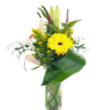 A tall, clear cylindrical vase filled with smooth river rocks holds a vibrant arrangement of flowers and greenery. At the center is a bright yellow gerbera daisy, surrounded by unopened pale pink lily buds, sprigs of goldenrod, long curved green leaves, and assorted leafy foliage, creating a modern, asymmetrical bouquet.