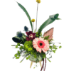 A low, round green ceramic vase on three small wooden legs contains an eclectic arrangement: a soft pink gerbera daisy at front right, a deep burgundy orchid nestled behind, bright yellow billy ball stems rising above, spiky blue thistle blooms to the left, a lime-green globe dianthus at center, and assorted greenery—including long curved blades of palm leaf, a dried blush-pink palm fan, and trailing burgundy amaranthus—creating a dynamic, textured bouquet.