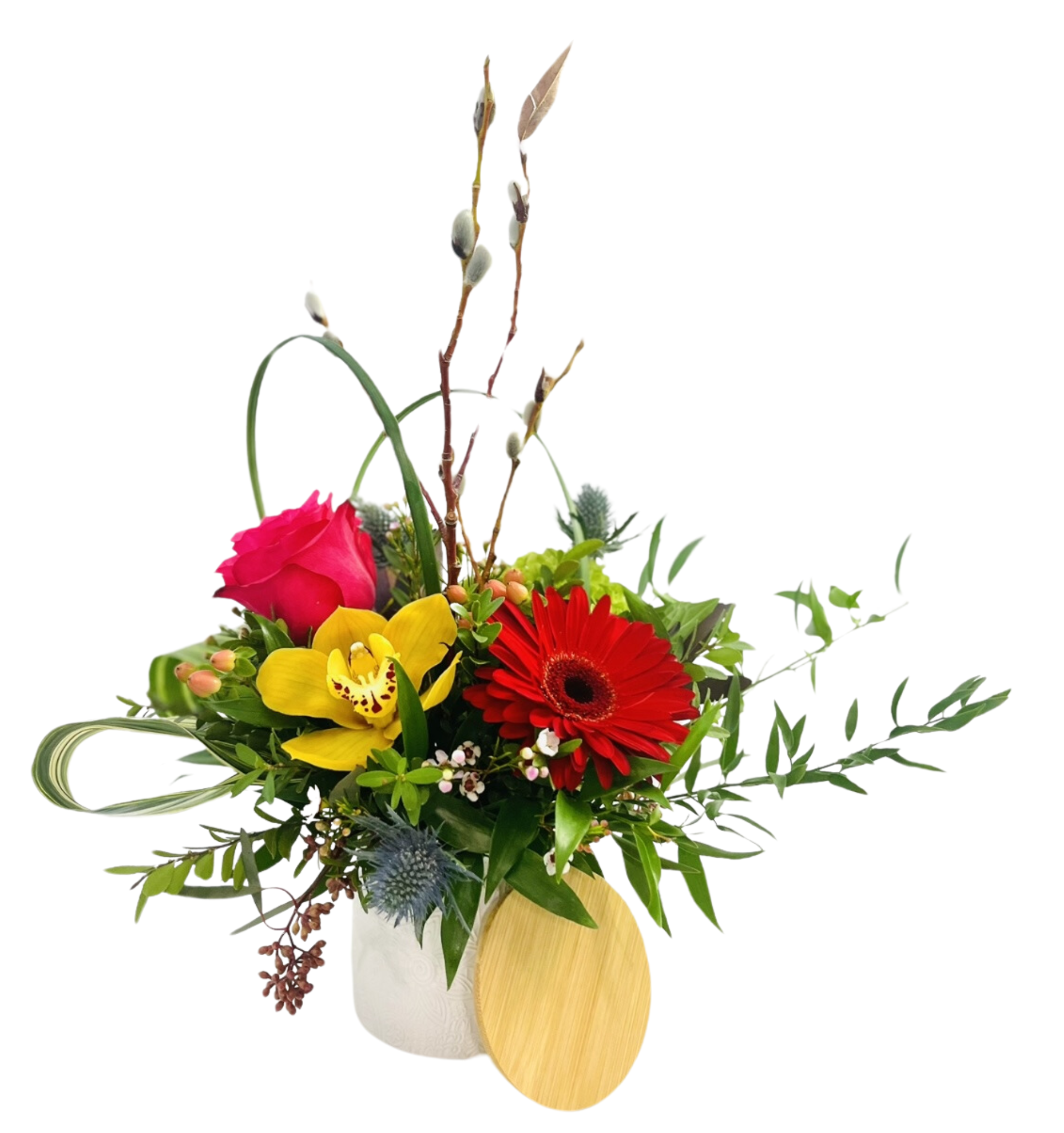 A cylindrical white ceramic vase holds a vibrant mixed bouquet. At center front is a bright red gerbera daisy, and to its left is a yellow orchid with burgundy‐speckled throat. Behind the orchid, a hot pink rose peeks out. Spiky blue thistles, small pink waxflower, and clusters of green hypericum berries fill gaps. Two tall pussy willow branches rise above, flanked by a looped variegated palm leaf on the left. Glossy eucalyptus and fine ferns trail over the rim on both sides. A round wooden lid rests against the vase’s base.