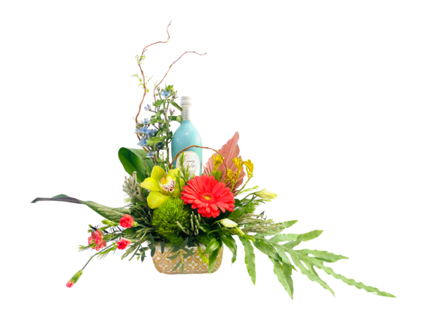 Rectangular tan-and-white patterned container holds a low, sprawling arrangement. A tall turquoise bottle sits toward the back amid twining curly willow branches. In front, a bright red gerbera, chartreuse pom-pom, and yellow orchid are surrounded by small pink buds, blue delphinium, and delicate greenery. Long, fern-like fronds extend horizontally on each side.