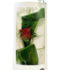 A single red rose bud wrapped in glossy green leaves and wispy fern stems, displayed upright inside a tall white gift box with a clear plastic window.