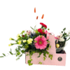 A rectangular pink gift box holds a lush mixed bouquet and a small ice bucket with champagne and chocolates. The arrangement features a large pink gerbera daisy at front center, clusters of red carnations and pale yellow spray carnations to the left, two pink orchids nestled above, blue thistle accents, and tall stems of orange bunny tail grass rising behind. Greenery, including trailing vines and eucalyptus, spills over the box’s edges. On the right side, a clear ice bucket cradles a bottle of sparkling wine and three gold-wrapped Ferrero Rocher chocolates, tied with a pink “Mother’s Day” ribbon.