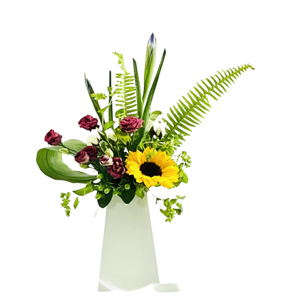 A tall, white tapered vase holds an asymmetrical floral arrangement featuring a large yellow sunflower at center right; clustered deep burgundy spray roses; unopened blue iris and lily buds rising above; delicate pink waxflower; bright green fern fronds; and a single large, curved leaf, all interspersed with assorted greenery.