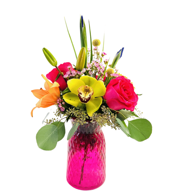 A bright pink, diamond-patterned glass vase holds a colorful bouquet featuring a central yellow orchid with burgundy markings, a hot pink rose, an orange lily, small clusters of pink waxflowers, yellow billy balls, unopened lily and iris buds, and sprigs of eucalyptus and greenery.